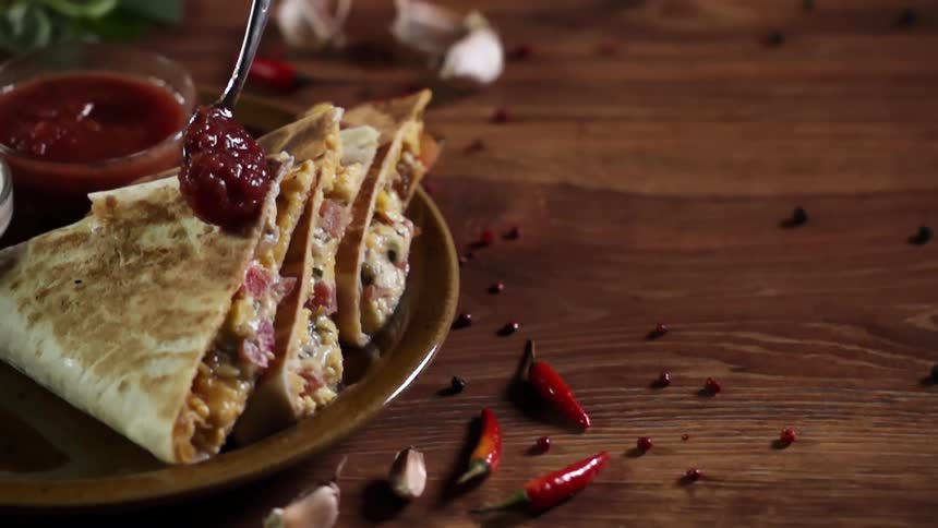 A spoonful of sauce pours onto a stack of quesadillas on a plate