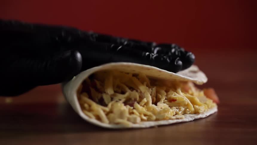 Person wearing black gloves folds tortilla over on cheese covered filling