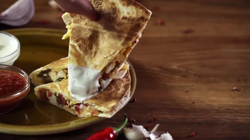 A quesadilla wedge dipped in sour cream is placed on a plate on top of two other wedges
