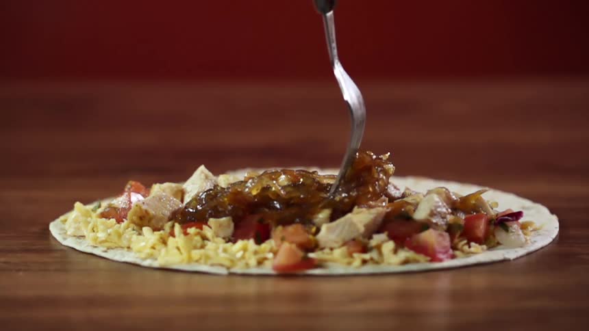 A fork spreading sauerkraut over meat and vegetables on a flatbread on a table