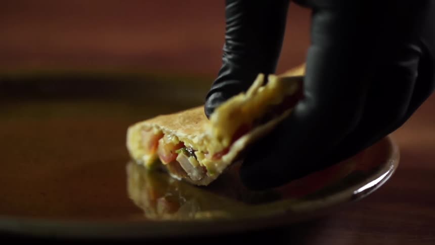 A gloved hand places a slice of quesadilla on a round tray