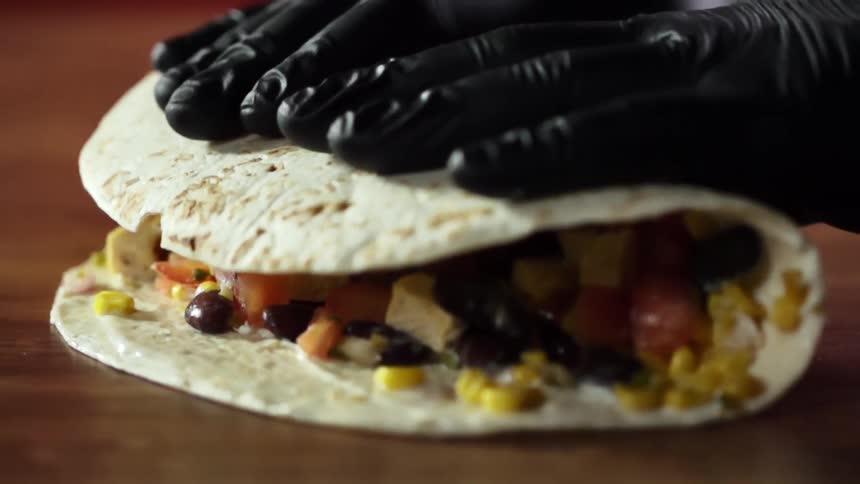 A soft taco filled with chicken beans and corn is being folded closed