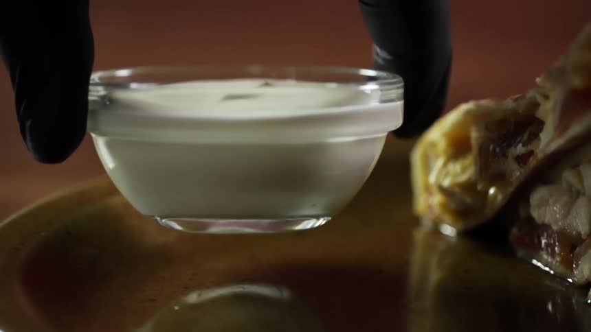 A person puts a bowl with sauce on a plate with food
