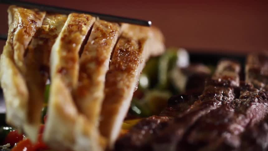 Chicken sliced into strips is placed in a pan next to strips of steak on top of colorful peppers