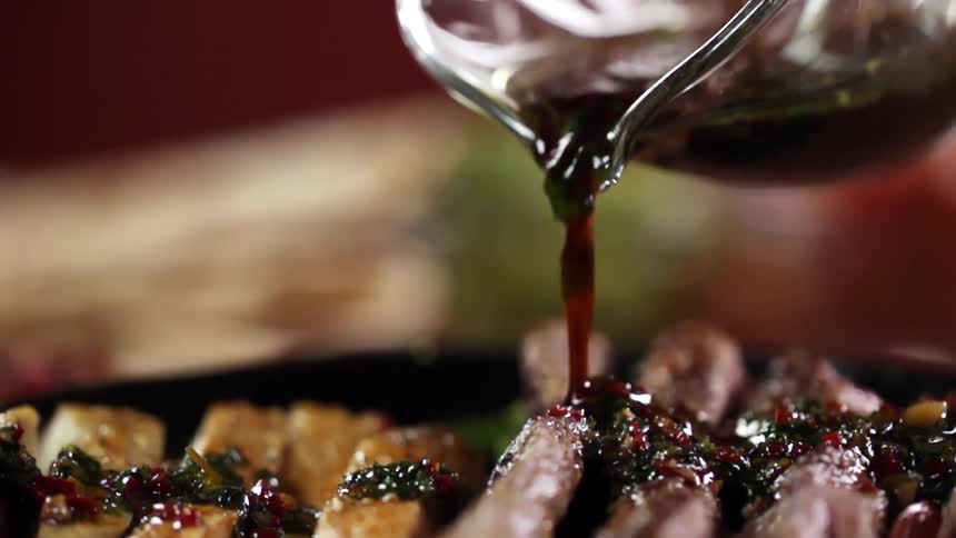 Sauce being poured onto a pan with steak chicken and vegetables
