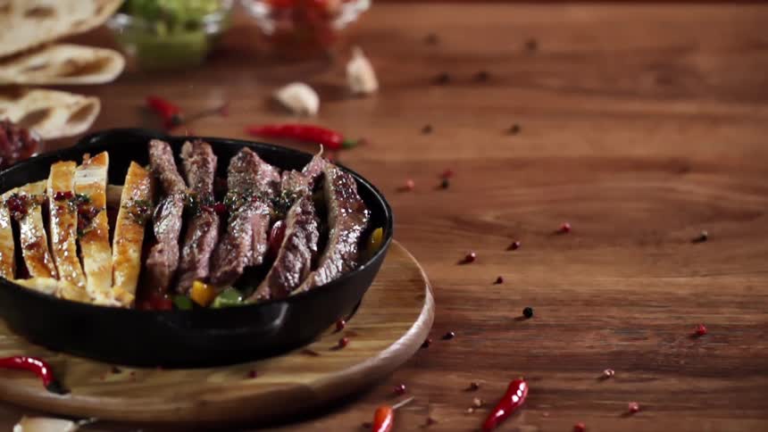 Seasoning is added to chicken and beef fajitas in iron skillet