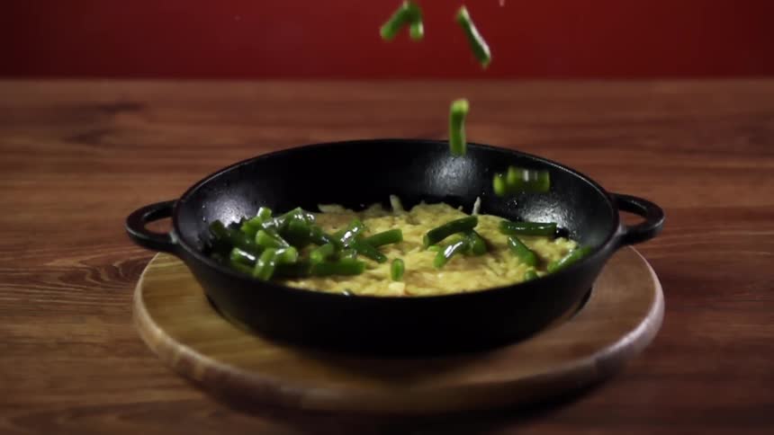 Green beans falling on noodles in a cast iron pot over a round board