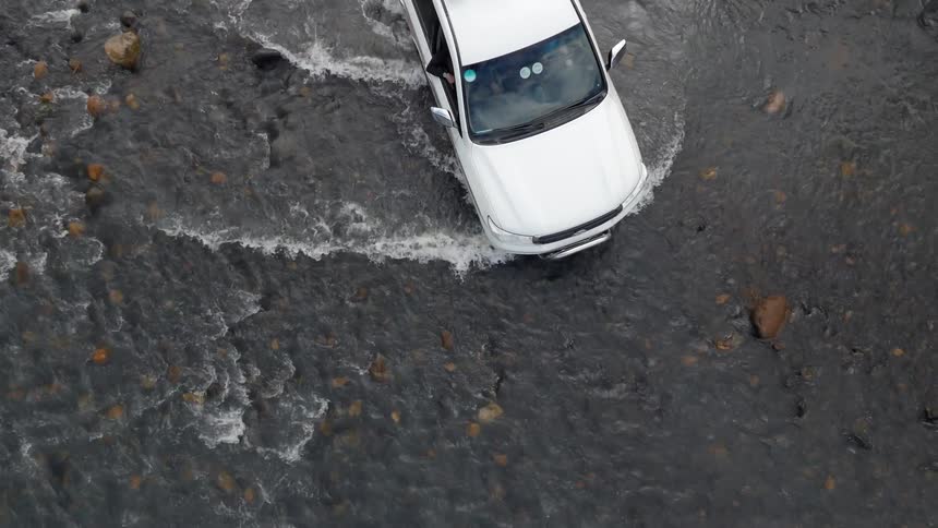 A white vehicle drives through a shallow river