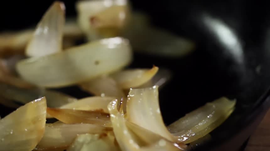 Sliced sauteed onions are dropped into a black pan