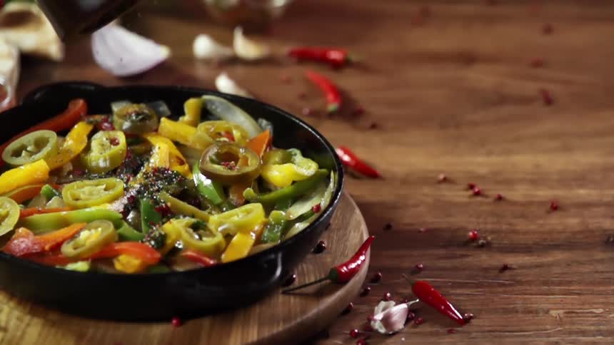 Seasoning falling over cooked vegetables inside a cast iron pan over a wooden table