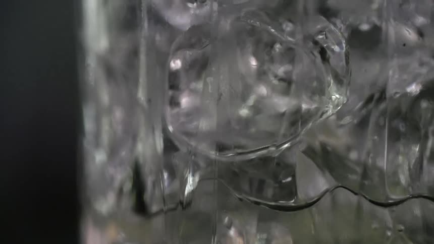 An alcoholic drink being poured in to a glass with ice