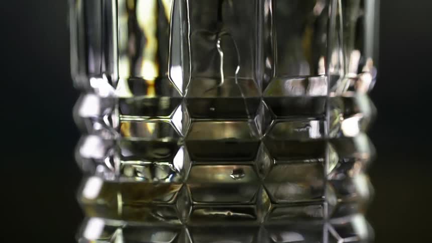 Alcoholic beverage is poured into a glass standing out against the dark background