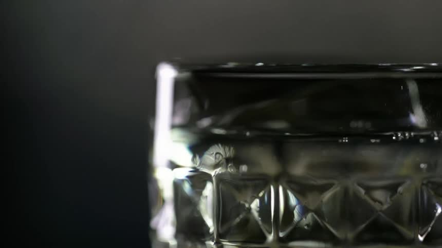 A drinking glass full of a beverage has a few more drops falling into it
