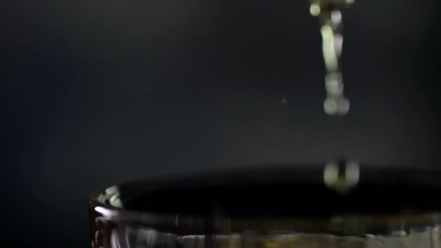 A glass is being overfilled with alcoholic beverage