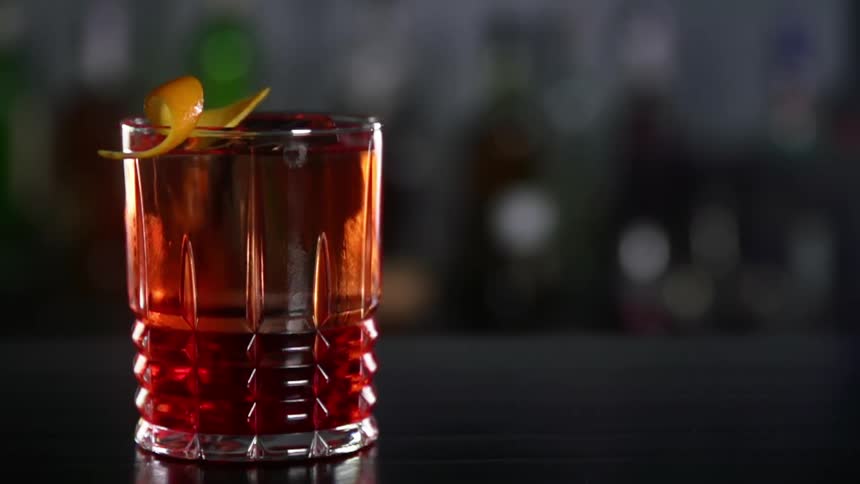 Orange peel falls on a glass filled with alcoholic beverage and ice