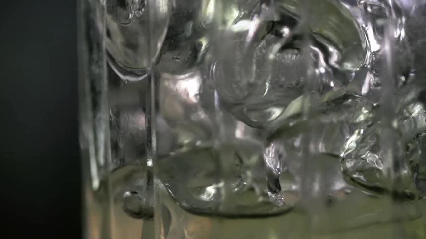 Alcoholic beverage being poured into a glass filled with ice