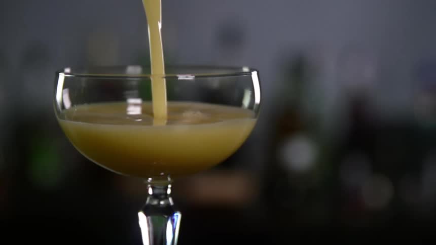 A yellowish alcoholic beverage being poured into a glass in front of bottles