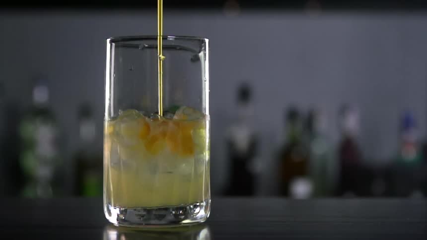 Yellow thick syrop is being poured into a glass in a bar