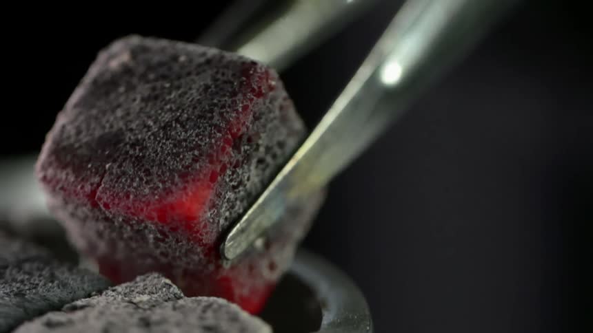 A person sets a heated charcoal cube into a metal ring