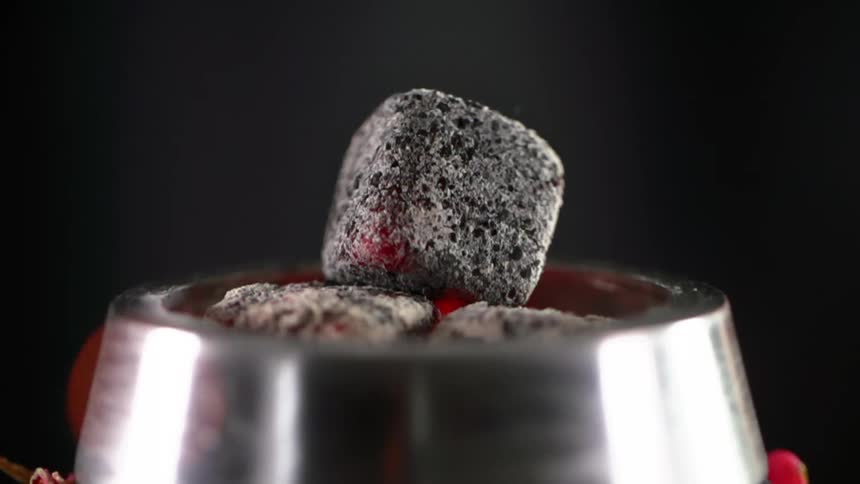 Heated charcoal cubes in a stainless steel bowl as flame and embers rise