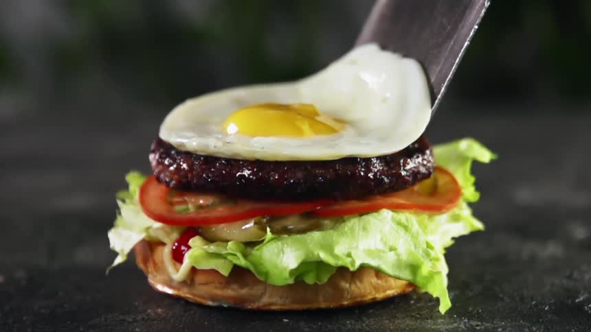 A fried egg sliding from a spatula onto the burger patty