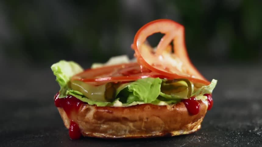 Tomato slices drop over lettuce and pickles on a hamburger bun