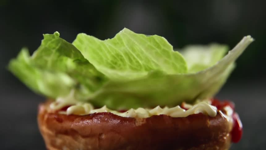 Slice of lettuce falling onto a bun with spread over it