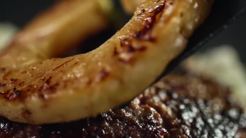 Grilled pineapple sliced is placed atop hamburger patty using a spatula