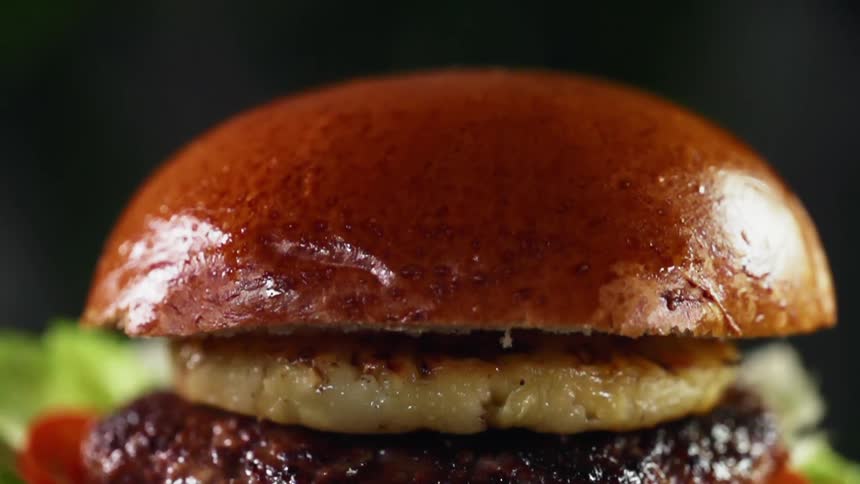 A top of a bun falling onto a grilled pineapple placed on a burger patty