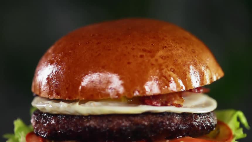 Top of brioche hamburger bun falls and lands on top of hamburger patty covered with a fried egg