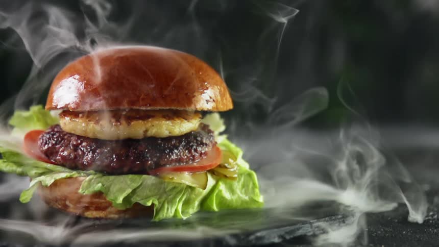 Gourmet hamburgerwith a slice of grilled pineapple  surrounded by smoke