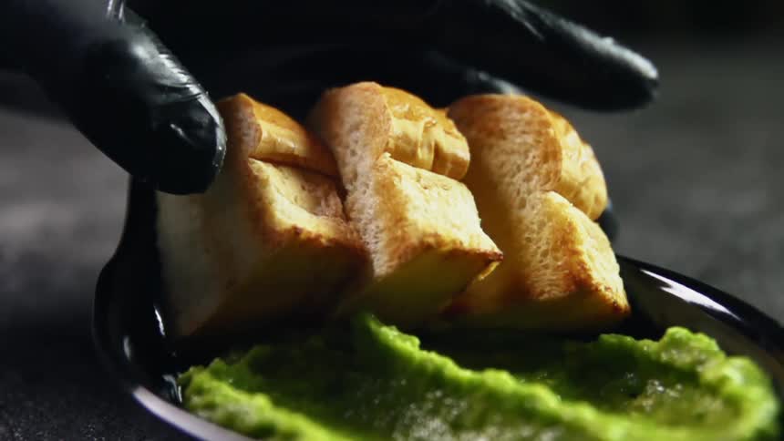 Cook puts small slices of toasted bread next to guacamole on a black plate