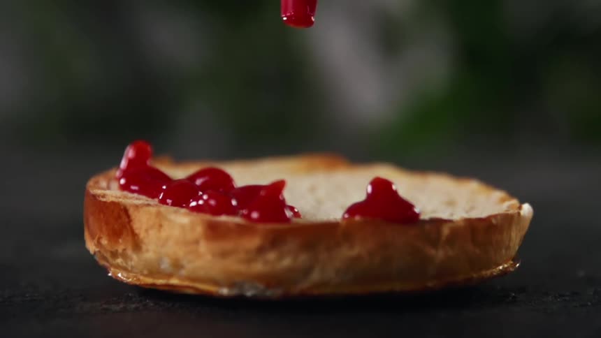 A bread bun with ketchup being poured onto it