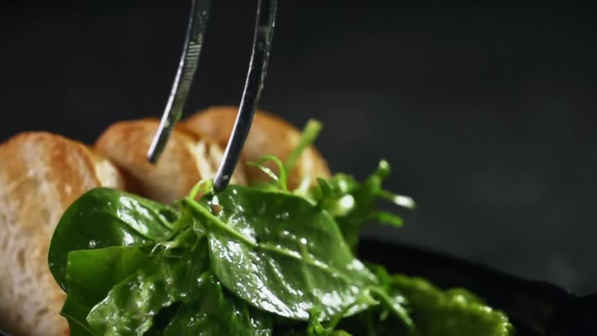 Tongs add leafy salad to plate with bread and guacamole
