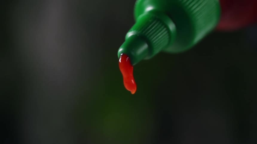 A red condiment dripping from the nozzle of a bottle