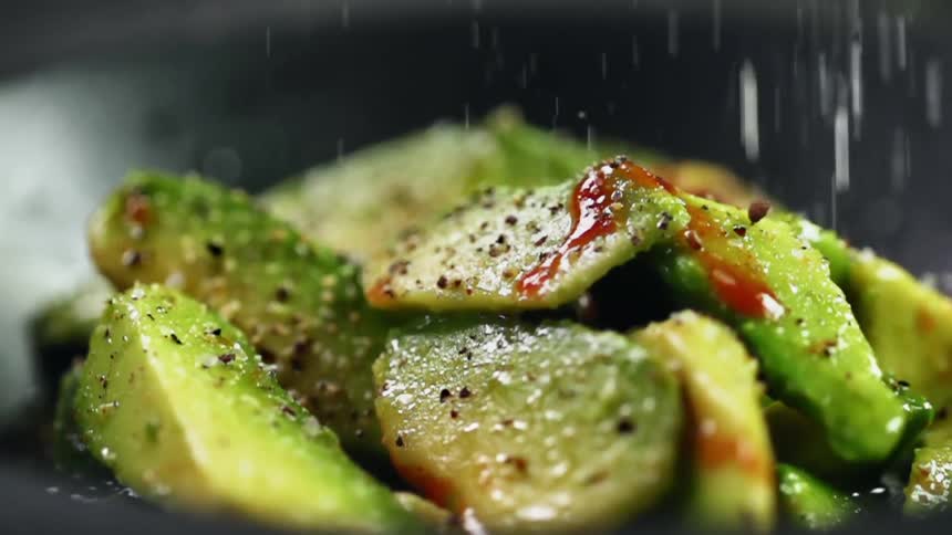 Salt is added to avocado slices in black bowl