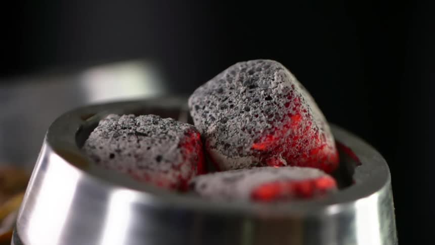 Three small pieces of charcoal are slightly burning in a metal ring and releasing small embers into the air