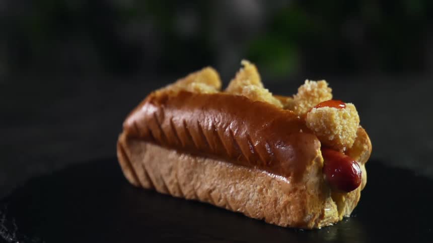Ketchup is being dripped onto a hot dog with tiny nuggets in a bun