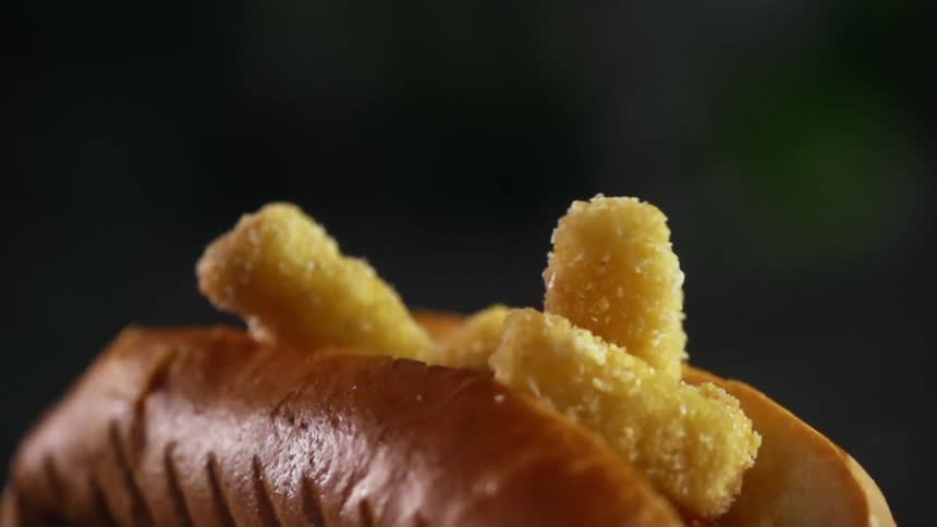 Tiny fried nuggets falling inside an opened hot dog bun