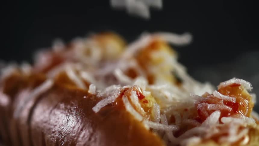 Shredded cheese is sprinkled over the top of an open hot dog