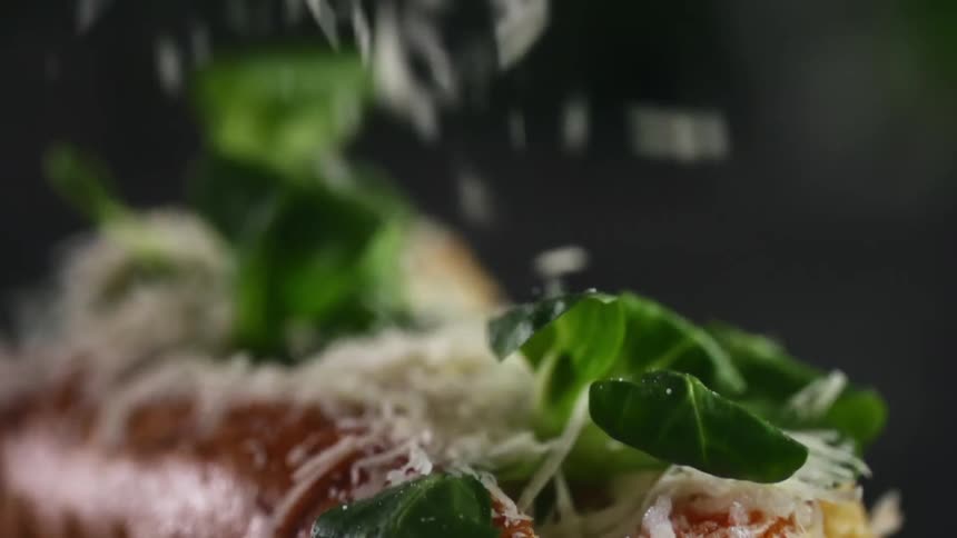 Grated cheese falling over a hot dog bun filled with green leafy vegetables