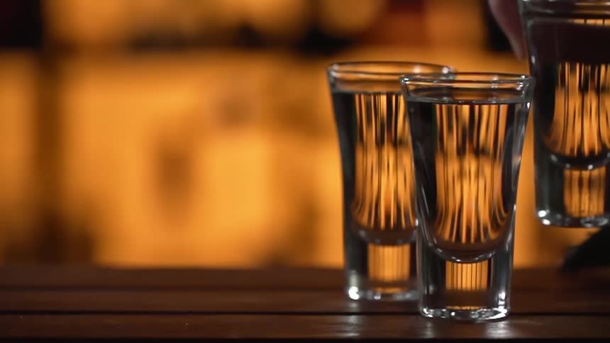 Person picks up shot glass from wooden paneled surface