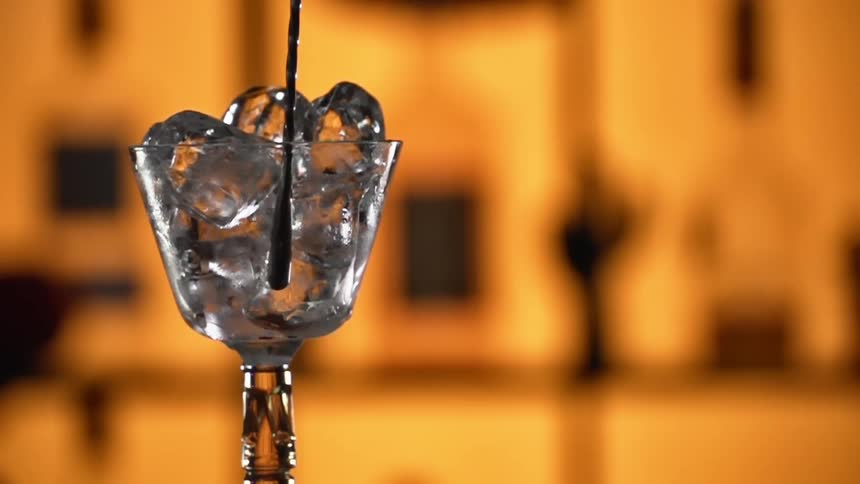 Ice cubes being stirred in a drinking glass with a mixing spoon