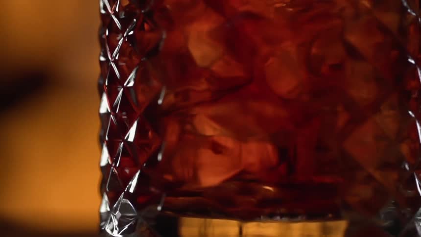 Alcoholic drink being stirred with ice inside a glass over a counter