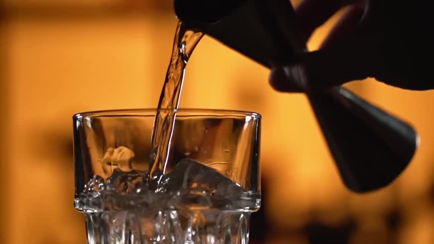 Jigger pouring alcohol in a glass over ice