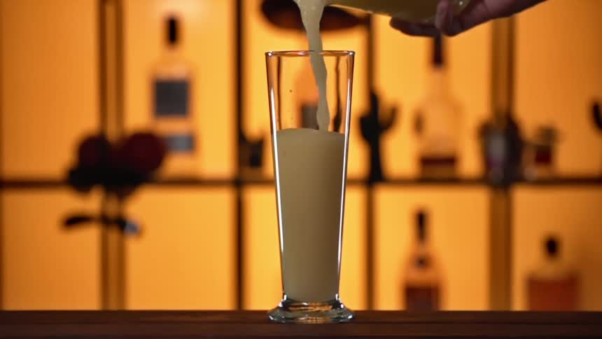 A bartender pours a frozen blended drink into a glass on a bar counter