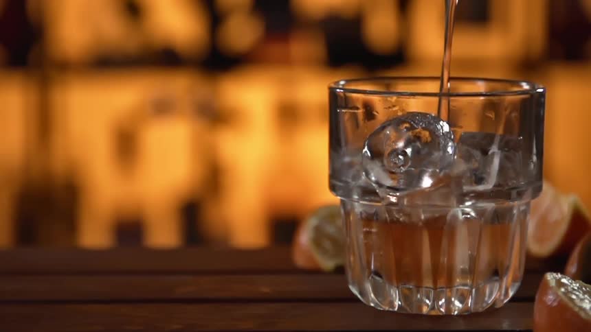 Liquid is poured into a small glass containing ice cubes atop the counter in a bar