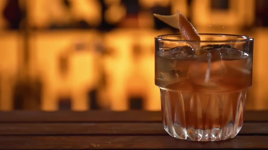 Citrus rind falls into a glass containing beverage and ice cubes