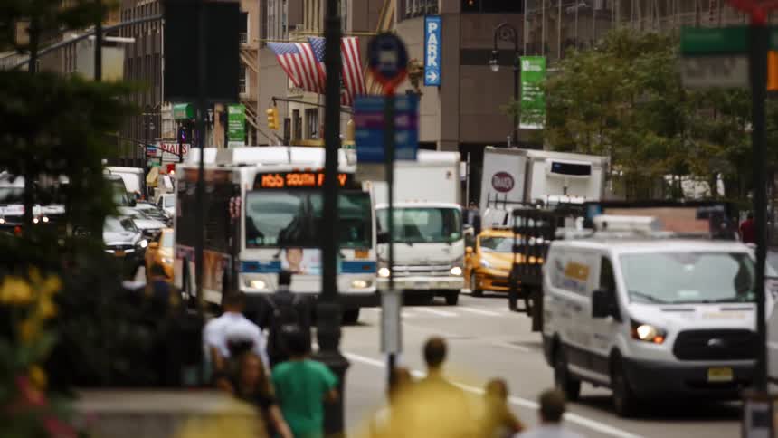 Cars drive down a busy city street as people walk along