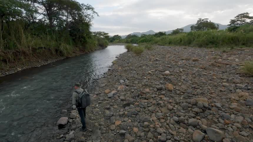 A man is hiking along a stream on a cloudy day